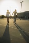 Romantique jeune couple flânant main dans la main à travers un parking vide — Photo de stock
