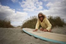 Senior woman on beach, waxing surfboard — Stock Photo