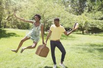 Coppia giovane con cestino da picnic in parco, con salto femminile a mezz'aria — Foto stock