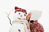 Woman kissing snowman at winter — Stock Photo