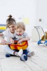Hermano y hermana tocando guitarra de juguete en casa - foto de stock