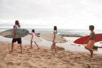 Four young friends carrying surfboards on beach — Stock Photo