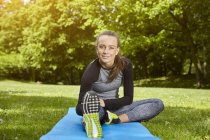 Молода жінка тренується в парку, тягнеться на тренувальний килимок — стокове фото