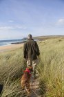 Man walking pet dog on sand dunes, Constantine Bay, Cornwall, UK — Stock Photo