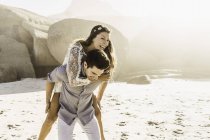 Uomo dando fidanzata un piggy indietro sulla spiaggia illuminata dal sole, Città del Capo, Sud Africa — Foto stock