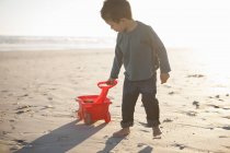 Мальчик тянет игрушечный грузовик заполненный песком вдоль пляжа — стоковое фото