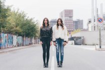 Portrait of twin sisters, in urban area, standing side by side — Stock Photo