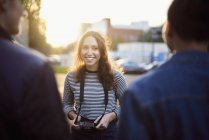 Sobre a vista do ombro da jovem mulher falando com amigos masculinos na rua iluminada pelo sol — Fotografia de Stock