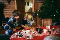 Dois irmãos abrindo presentes de Natal à mesa — Fotografia de Stock