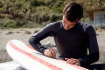 Jovem adulto surfista do sexo masculino encerando bordo — Fotografia de Stock