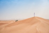 Young middle eastern man wearing traditional clothes looking out from desert dune, Dubai, United Arab Emirates — Stock Photo