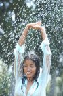 Retrato de mujer joven bajo la lluvia con los brazos levantados - foto de stock