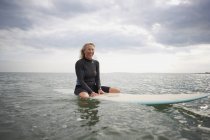 Portrait d'une femme âgée assise sur une planche de surf en mer, souriante — Photo de stock