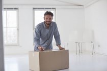 Portrait of young man writing on cardboard box whilst moving house — Stock Photo