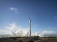 Windkraftanlage mit Sturmwellen an der Küste unter blauem Himmel — Stockfoto