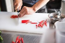 Imagem cortada do homem cortando pimentas vermelhas — Fotografia de Stock