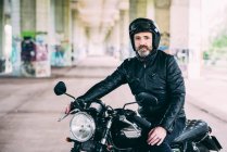 Зрілий чоловічий мотоцикліст сидить на мотоциклі в аварійному шоломі під літаком — стокове фото