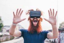 Portrait de jeune hipster masculin aux cheveux roux et à la barbe criant tout en portant un casque de réalité virtuelle — Photo de stock