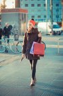 Mulher adulta média vestindo chapéu pom pom vermelho passeando com sacos de compras — Fotografia de Stock
