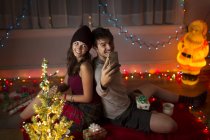 Jeune couple prenant selfie dans le salon à Noël — Photo de stock