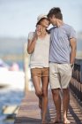 Young couple walking along jetty, arms around each other — Stock Photo