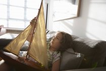 Girl lying on living room sofa with toy sailing boat — Stock Photo