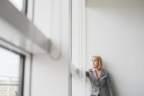 Reife Geschäftsfrau starrt durch Bürofenster nach oben — Stockfoto