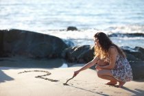 Женщина рисует вопросительный знак на песке — стоковое фото