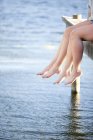 Two pairs of female legs dangling from pier — Stock Photo