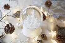 Рождественский стол со снежным шаром и еловыми шишками — стоковое фото