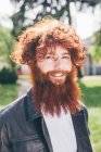 Retrato de jovem hipster masculino com cabelo encaracolado vermelho e barba no parque — Fotografia de Stock