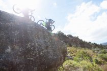 Pareja joven llevando bicicletas de montaña desde las rocas - foto de stock