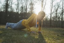 Young female runner doing warming push-ups in field — Stock Photo