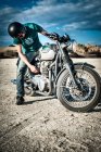 Hombre adulto medio comprobando motocicleta en llanura árida, Cagliari, Cerdeña, Italia - foto de stock