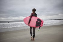 Вид сзади на женщину-серфингистку, несущую доску для серфинга в море на Рокавей Бич, Нью-Йорк, США — стоковое фото