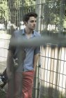 Grave giovane uomo con skateboard appoggiato sulla recinzione del parco — Foto stock