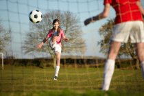Chica pateando pelota de fútbol en el gol - foto de stock