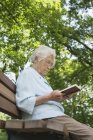 Senior mulher sentada no banco do parque leitura bíblia — Fotografia de Stock