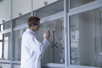 Junge männliche Wissenschaftlerin schreibt Ergebnisse auf Rauchschrankfenster — Stockfoto
