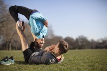 Молодая женщина балансирует на вершине человека практикуя йогу позы в парке — стоковое фото