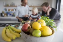 Primer plano de cuenco con fruta fresca en la mesa con la familia en el fondo - foto de stock