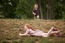 Girl rolling down hill, boy running — Stock Photo