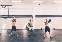 Three young male cross trainers training with kettlebells in gym — Stock Photo