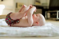 Baby girl lying on back playing with feet — Stock Photo