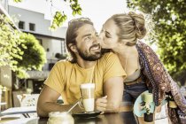 Young woman kissing boyfriend on cheek at sidewalk cafe, Franschhoek, South Africa — Stock Photo