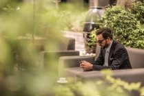 Uomo d'affari che legge i testi degli smartphone sul divano da giardino dell'hotel, Dubai, Emirati Arabi Uniti — Foto stock