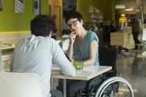 Donna in sedia a rotelle seduta al tavolo del ristorante con un amico — Foto stock