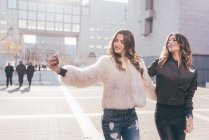 Twin sisters, walking outdoors, taking selfie, using smartphone — Stock Photo