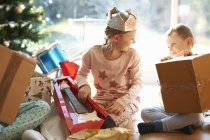 Boy and sister sitting on living room floor opening christmas gifts — Stock Photo