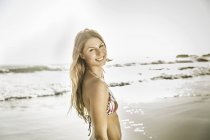 Porträt einer Frau mit Bikini-Oberteil, die am Strand von Kapstadt in Südafrika über die Schulter schaut — Stockfoto